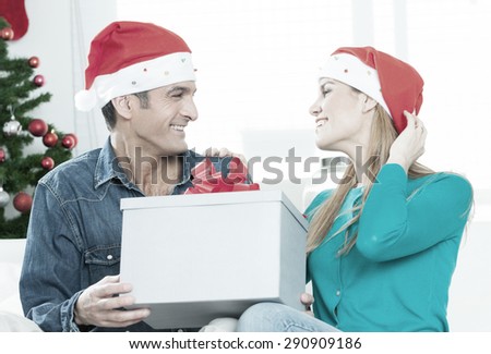 Christmas Gift. Happy Couple in Santa\'s Hat with Christmas and New Year Gift at Home. Smiling Family Together. Christmas tree.