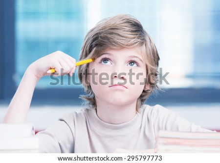 Elementary school boy at classroom desk trying to find new ideas for schoolwork.