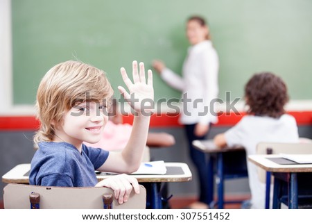 Education, elementary school, learning and people concept - group of school kids with teacher sitting in classroom and raising hand.