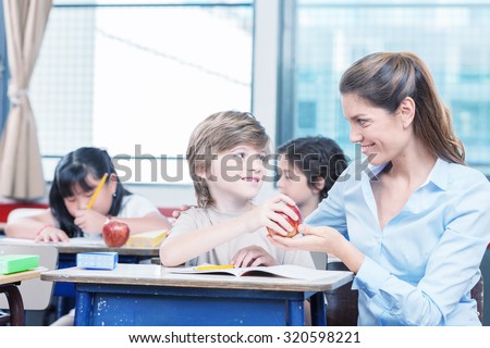 Kid handing red apple to teacher in elementary school.