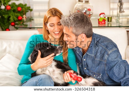 Happy wife and husband joking with their dog in home interior.