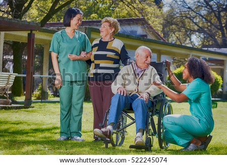 Afroamerican and asian nurses joking with elder people in hospital garden.