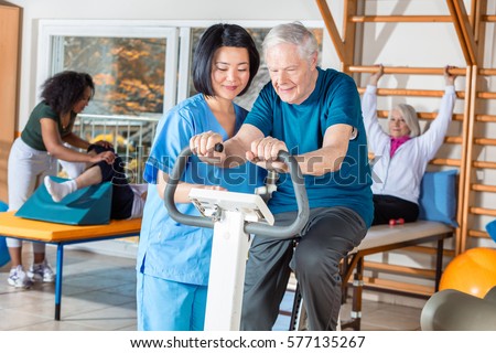 Asian nurse helping elder man in hospital gym.