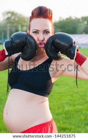 Pregnant young woman with boxing gloves on stadium