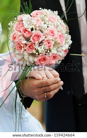 Bride and Groom holding Hands with Rings on Floral Bouquet