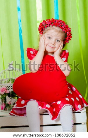 beautiful little girl in a red dress with a big red heart pillow