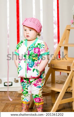 Baby girl in a fashionable suit, cap and rubber boots
