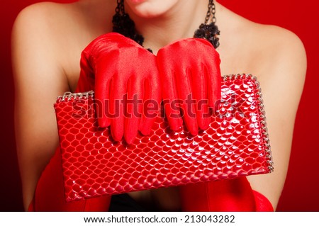 Female hands in red gloves holding a red clutch bag
