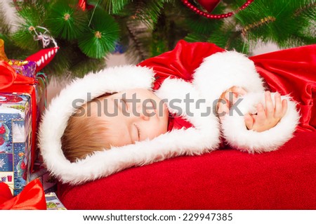 Baby in Santa costume sleeping at the Christmas tree