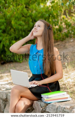 Teen girl works with the laptop in headphones and books sitting on the curb