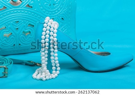 Beautiful blue shoes and handbag, pearls on blue background