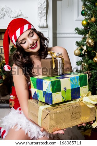 Beautiful young woman in Santa Claus clothes holding presents over Christmas background.