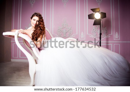 glamorous photo of a beautiful brunette bride in a luxurious wedding dress lying on pink sofa