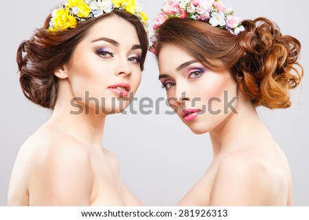Portrait of beautiful twins young women with perfect make-up and hair-style with flowers in hair