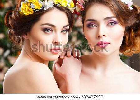 Portrait of beautiful twins young women with perfect make-up and hair-style with flowers in hair