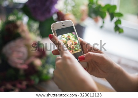Florist at work: pretty young blond woman making photo on her mobile phone (smart phone)