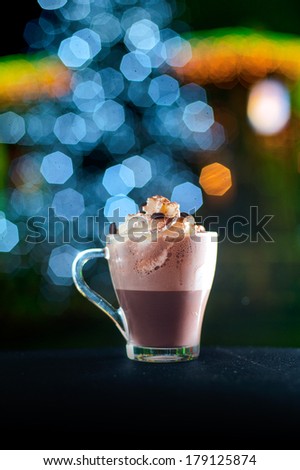 A glass of hot chocolate drink with whipped cream and chocolate chips and atmospheric bokeh lights in the background