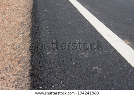 new asphalt road and white curb line, roadside with rock and soil material on new paved street