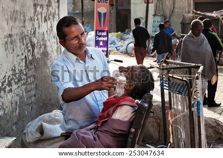 AMRITSAR, INDIA, DEC - 6, 2014: An unidentified street barber shaving a man on the street. A lot of Indian poor people shave with a straight razor on the streets in India.