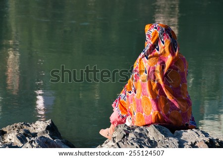 RISHIKESH, INDIA - DEC 10, 2014: Unidentified Indian woman in sari sits on a rock at the River Ganga. Rishikesh is  World Capital of Yoga,  has numerous yoga centres that also attract tourists