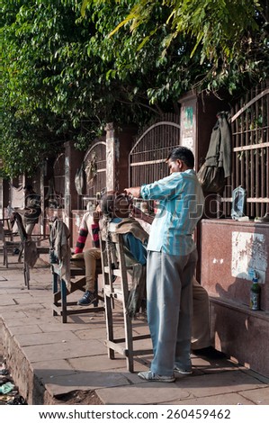 AGRA, INDIA - DEC 16, 2014: An unidentified street barbers shaving men on the street in market.  A lot of Indian poor people shave with a straight razor on the streets in India