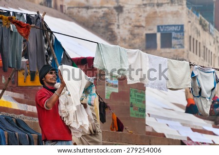 VARANASI, INDIA - DEC 23, 2014: Unidentified Indian man hang the wash on clothesline on ghat near sacred river Ganges in Varanasi. Uttar Pradesh, India