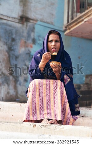 VARANASI, INDIA - DEC 23, 2014: Unidentified Indian woman eating a meal on the ghat near sacred river Ganges in Varanasi. Uttar Pradesh, India