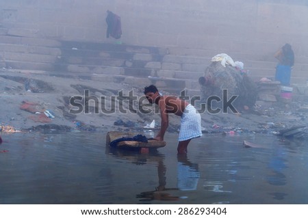 VARANASI, INDIA - DEC 24, 2014: Unidentified Indian man washes clothes in the holy water of the river Ganges at cold foggy winter morning. Varanasi. Uttar Pradesh, India
