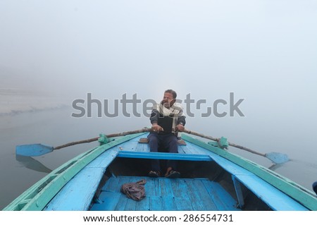 VARANASI, INDIA - DEC 24, 2014: Unidentified Indian man sailing on the boat on sacred river Ganges at cold foggy winter morning. Varanasi. Uttar Pradesh