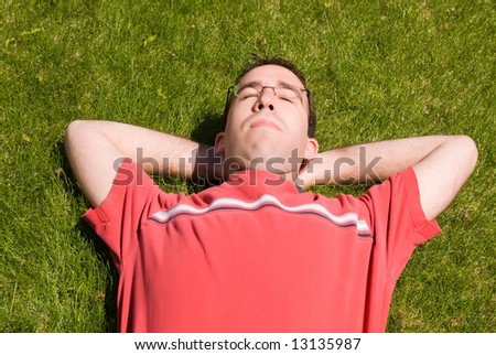 A young man wearing glasses, lying on the grass, relaxing in the sun