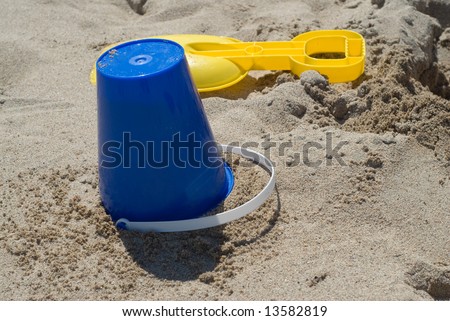 A blue pail and yellow shovel sitting on a sandy beach