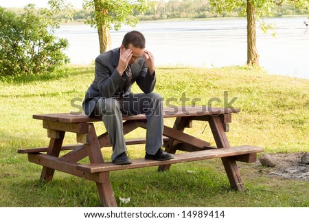 A young business worker sitting on a picnic table massaging his temples