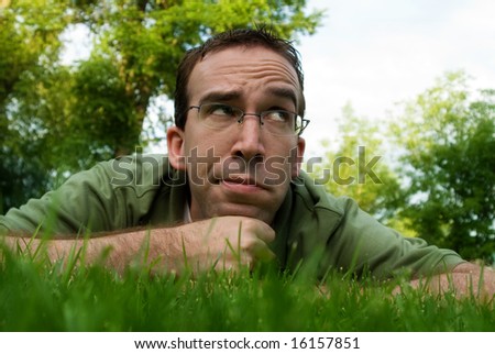 A young man lying in the grass and thinking outside