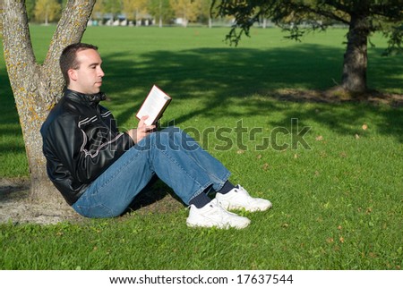 A young man reading a novel outside