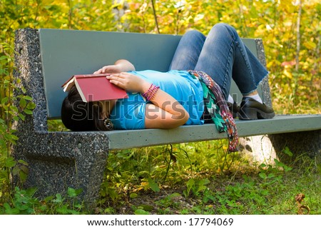 A nine year old girl lying on a park bench, with a book over her face