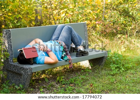 A young girl sleeping on a park bench outside