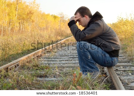 A sad man sitting on a set of railroad tracks doing some thinking