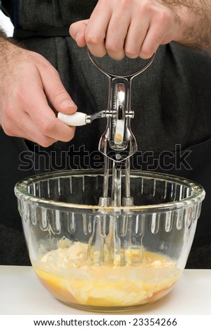 A young chef using a hand beater to mix some cookie batter