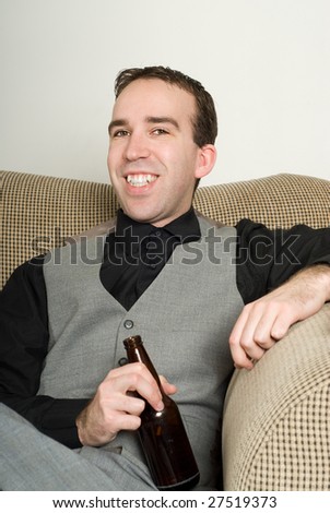 A smiling man wearing a suit is enjoying a beer at home, while sitting on the sofa