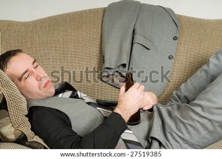A tired businessman lying on a sofa and having a beer