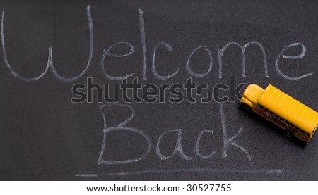 A black board with the words welcome back, and also a small toy school bus