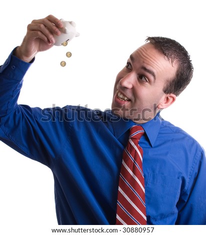 A young businessman emptying out his piggy bank that had some loose change in it, isolated against a white background