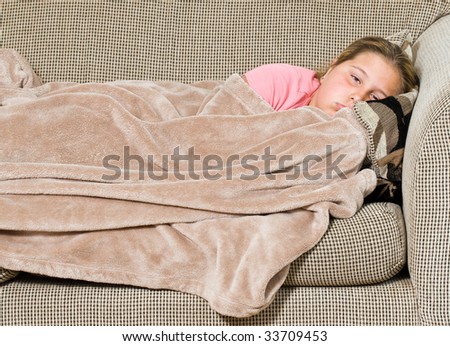 A young girl is covered with a blanket on the sofa and about to take a nap