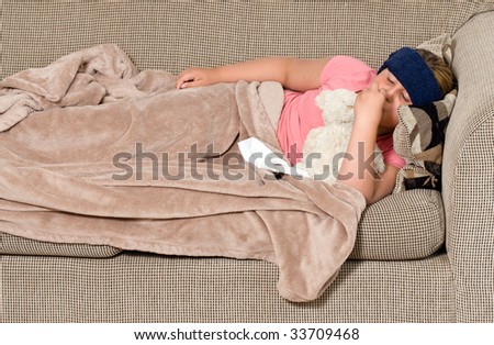 A young girl lying on the sofa feeling under the weather, and enjoying the company of her teddy bear