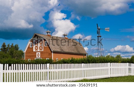 A old red barn along with a weather vane shot behind a white picket fence