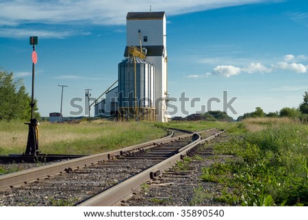 Prairie railroad tracks running along beside a tall grain elevator and vanishing in the distance