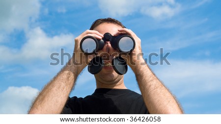 A young man looking at the viewer with a set of binoculars, with a blue sky behind him
