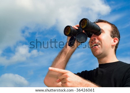A man bird watching with a set of binoculars and is pointing with his finger