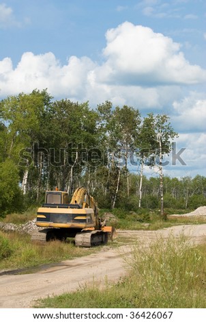 An excavator parked on the side of a gravel road near a job site