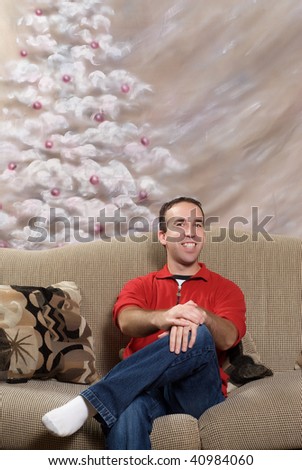 A smiling metrosexual man sitting on a sofa in front of a hand painted christmas tree